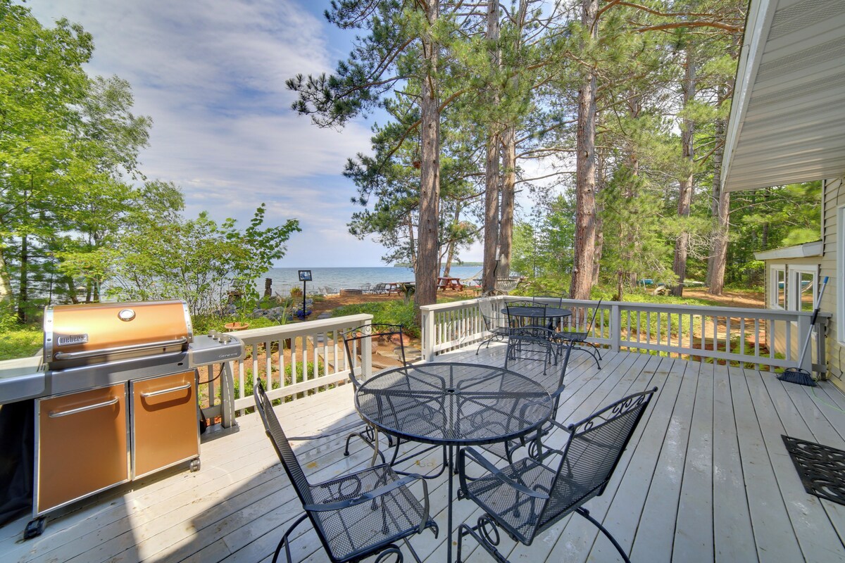 A deck with a grill, outdoor table, and chairs, overlooking a body of water.