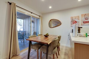 A dining area with a wooden table and chairs, a sliding glass door leading to an outdoor deck, and a kitchen area with a coffee maker and a mirror on the wall.