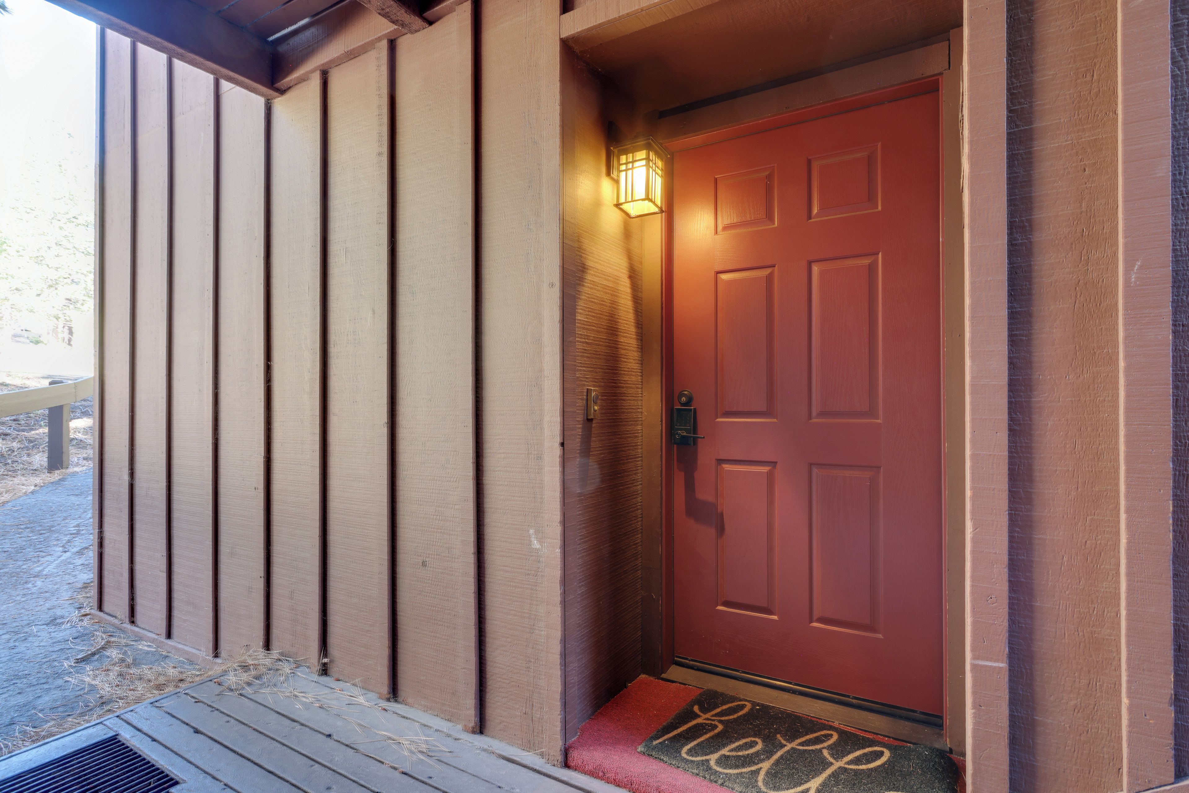 A wooden door with a red doorbell and a light fixture above it.
