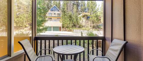A covered outdoor seating area with a table and four chairs, overlooking a residential area with houses and trees.