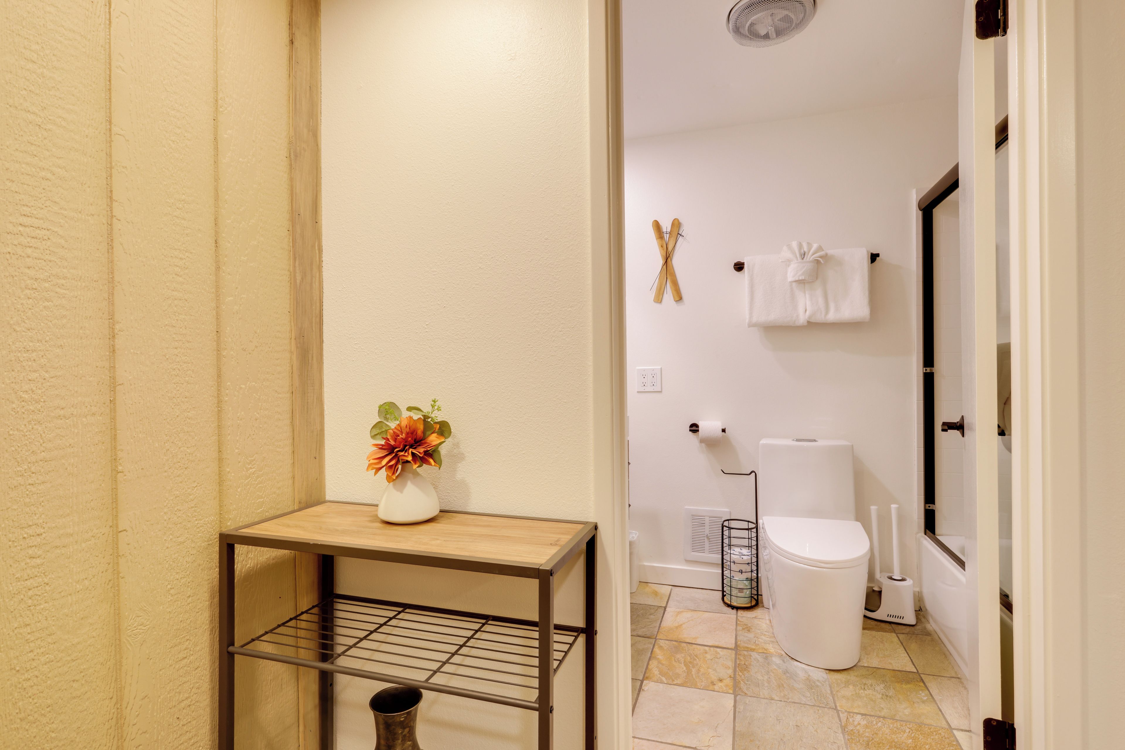 A bathroom with a shower, toilet, and a small table with a vase.