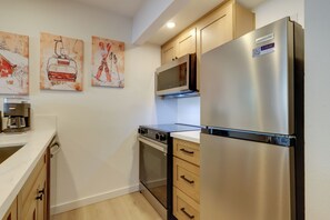 A modern kitchen with stainless steel appliances, wooden cabinets, and artwork on the wall.