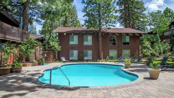 A swimming pool with a brick deck, surrounded by lounge chairs and potted plants.