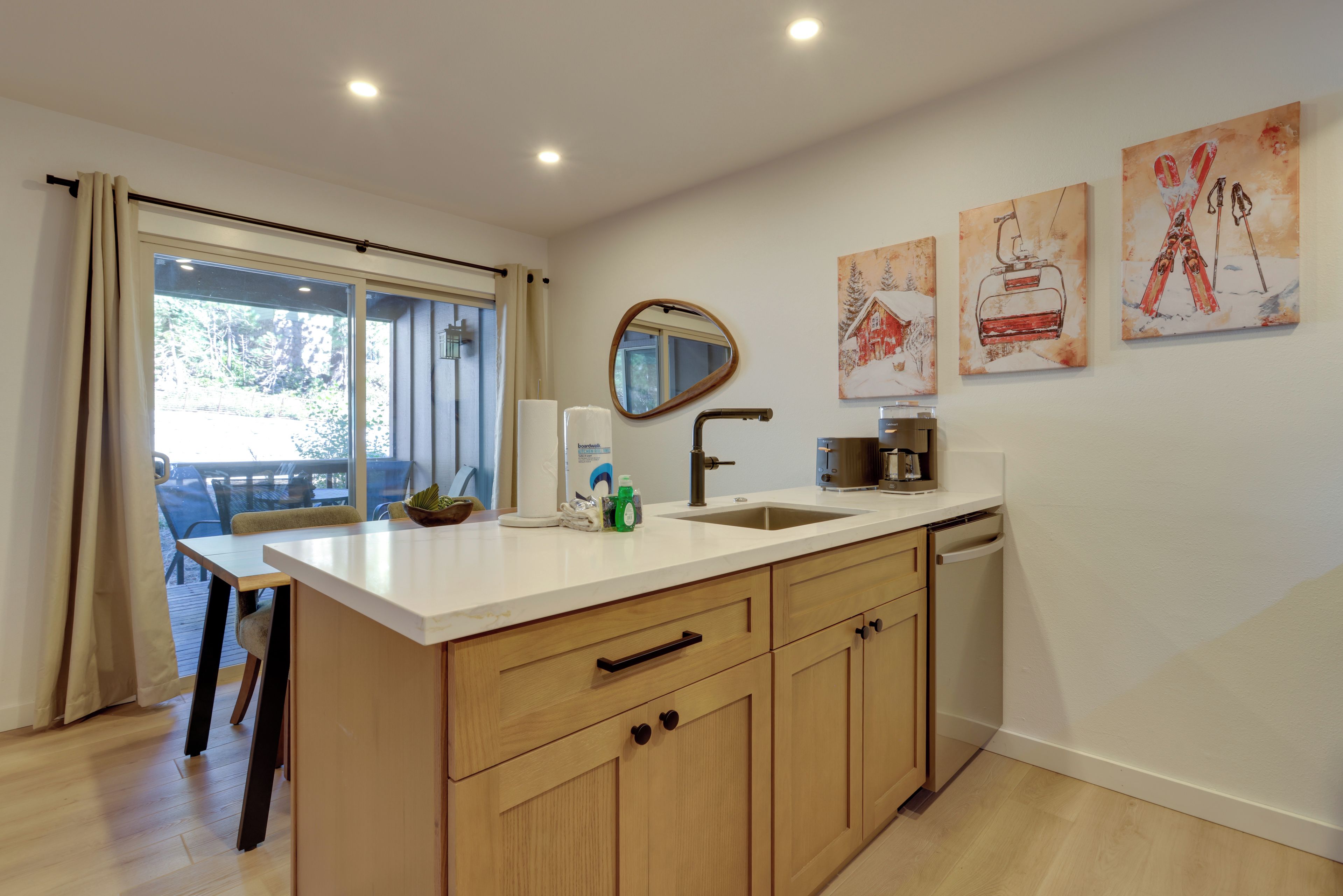 A modern kitchen with a large island, a built-in dishwasher, and a window overlooking a deck.