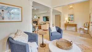 A living room with two blue armchairs, a small round table, and a wicker basket. There is a painting on the wall and a television in the background. - 30A Poolside Oasis: 2 Mi to Beach & Boat Access (Santa Rosa Beach)