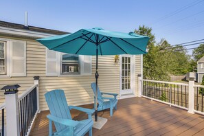 A wooden deck with two blue Adirondack chairs and a turquoise umbrella.