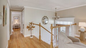 A spacious hallway with wooden flooring, a white railing, and a staircase leading to a landing with a lamp and a potted plant.