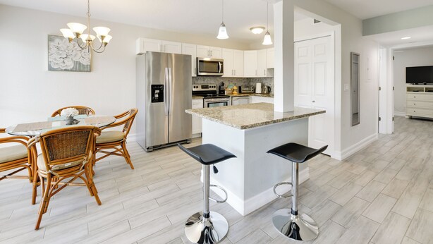 A modern kitchen with white cabinets, stainless steel appliances, and a central island with bar stools. - 3 Mi to Siesta Key Beach: Condo w/ Heated Pool! (Sarasota)