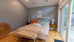 A bedroom with a bed, bedside tables, a large window, and a wall-mounted artwork.