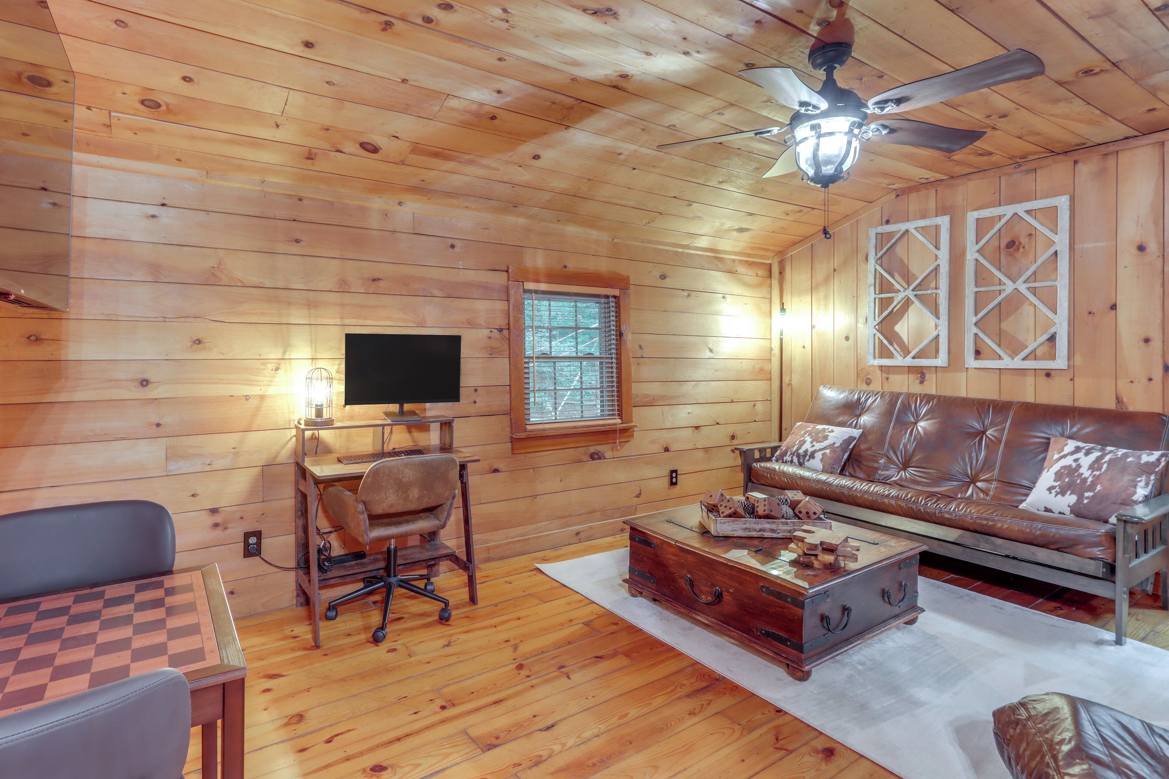 A wooden-paneled room with a leather sofa, a wooden coffee table, a desk with a computer, and a ceiling fan.