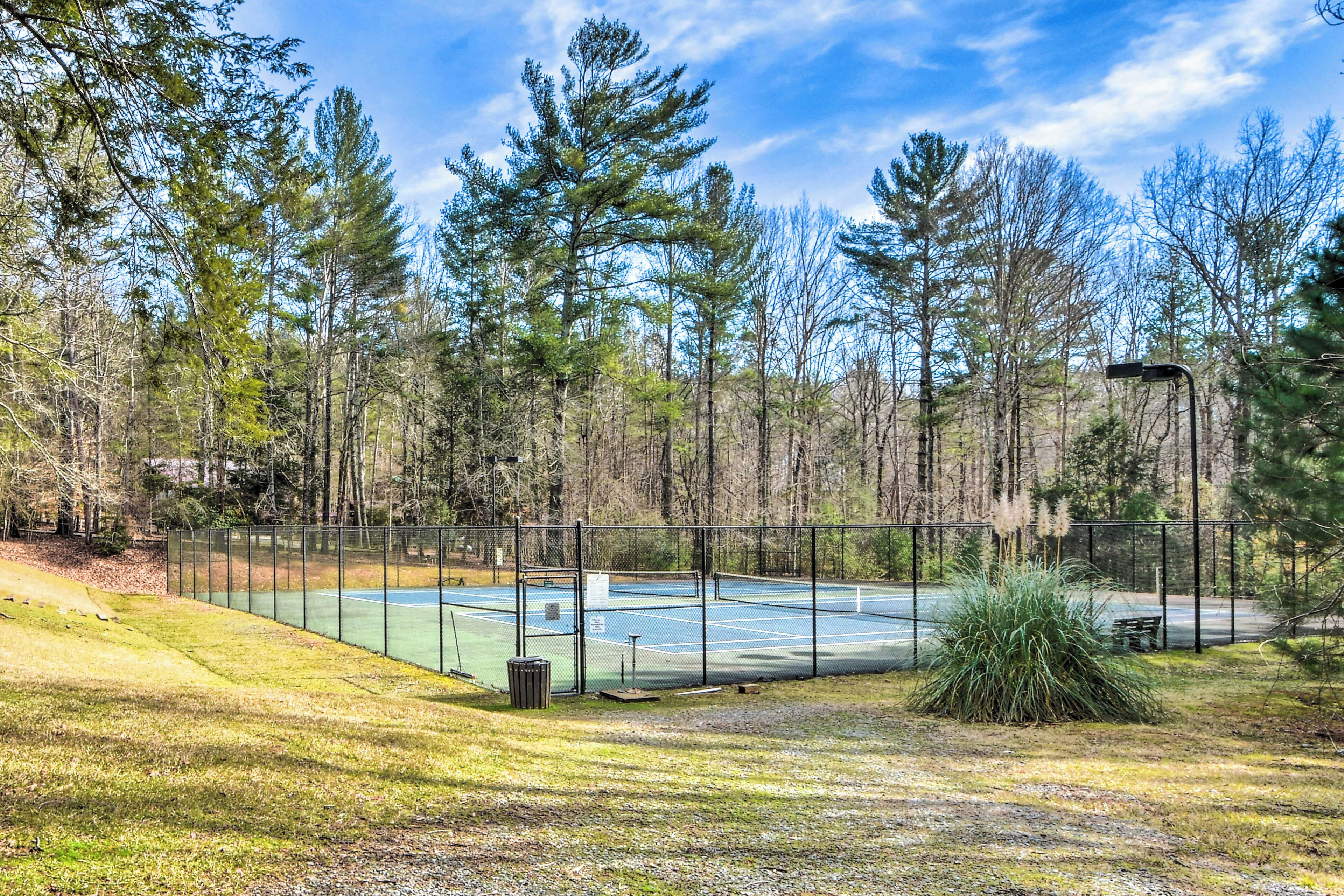 A tennis court surrounded by a forested area with a metal fence.
