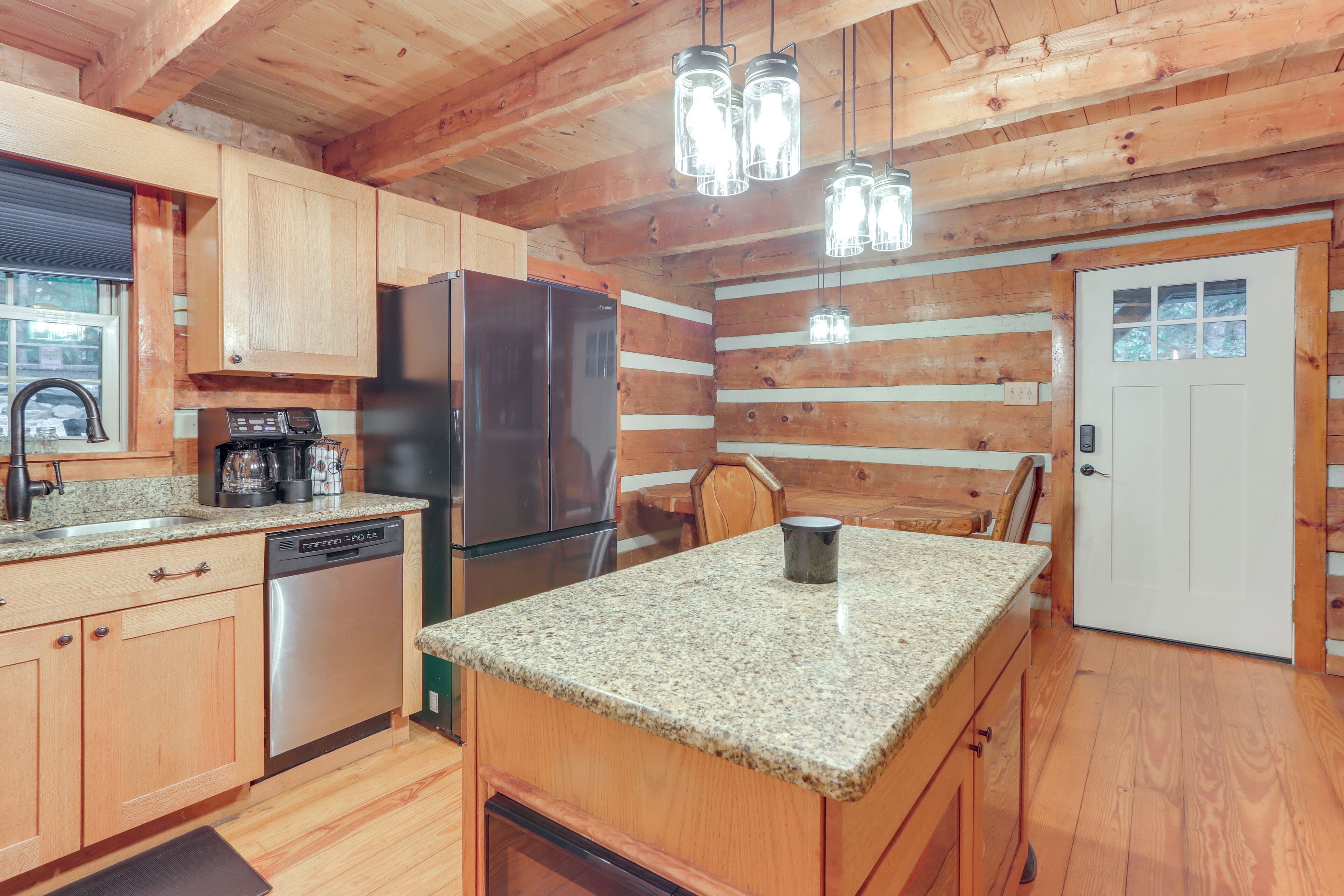 A kitchen with wooden cabinets, granite countertops, stainless steel appliances, and hanging light fixtures.