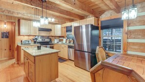 A wooden cabin interior with a kitchen featuring a stainless steel refrigerator, wooden cabinets, granite countertops, and hanging light fixtures. - Escape to the Mountains: Hot Tub Haven in Ellijay! (Ellijay)