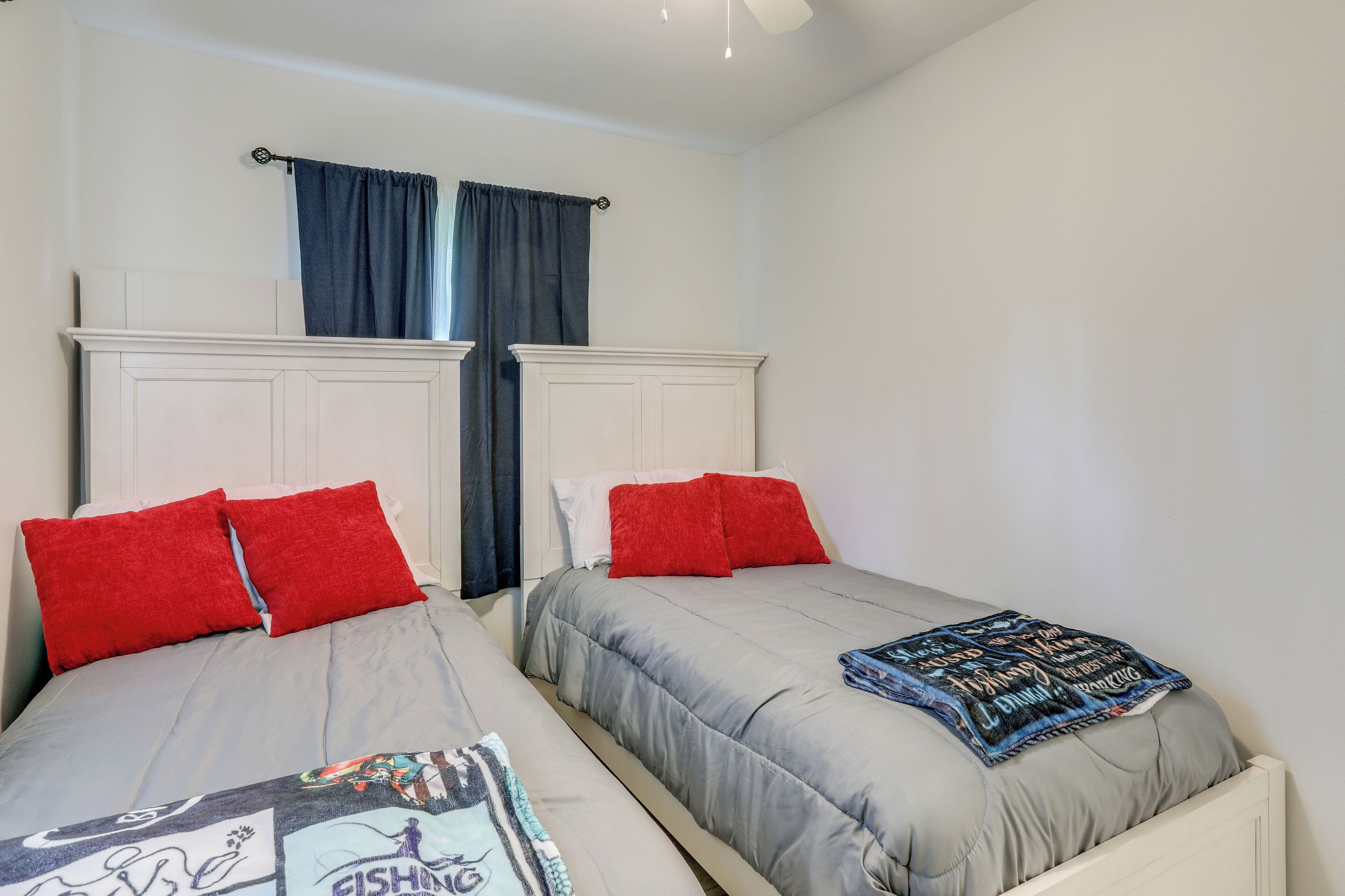 Two single beds with red pillows and grey bedding, a white headboard, and a dark blue curtain.