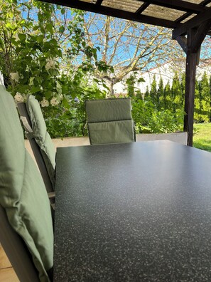 An outdoor patio with a table and chairs, surrounded by greenery and trees.