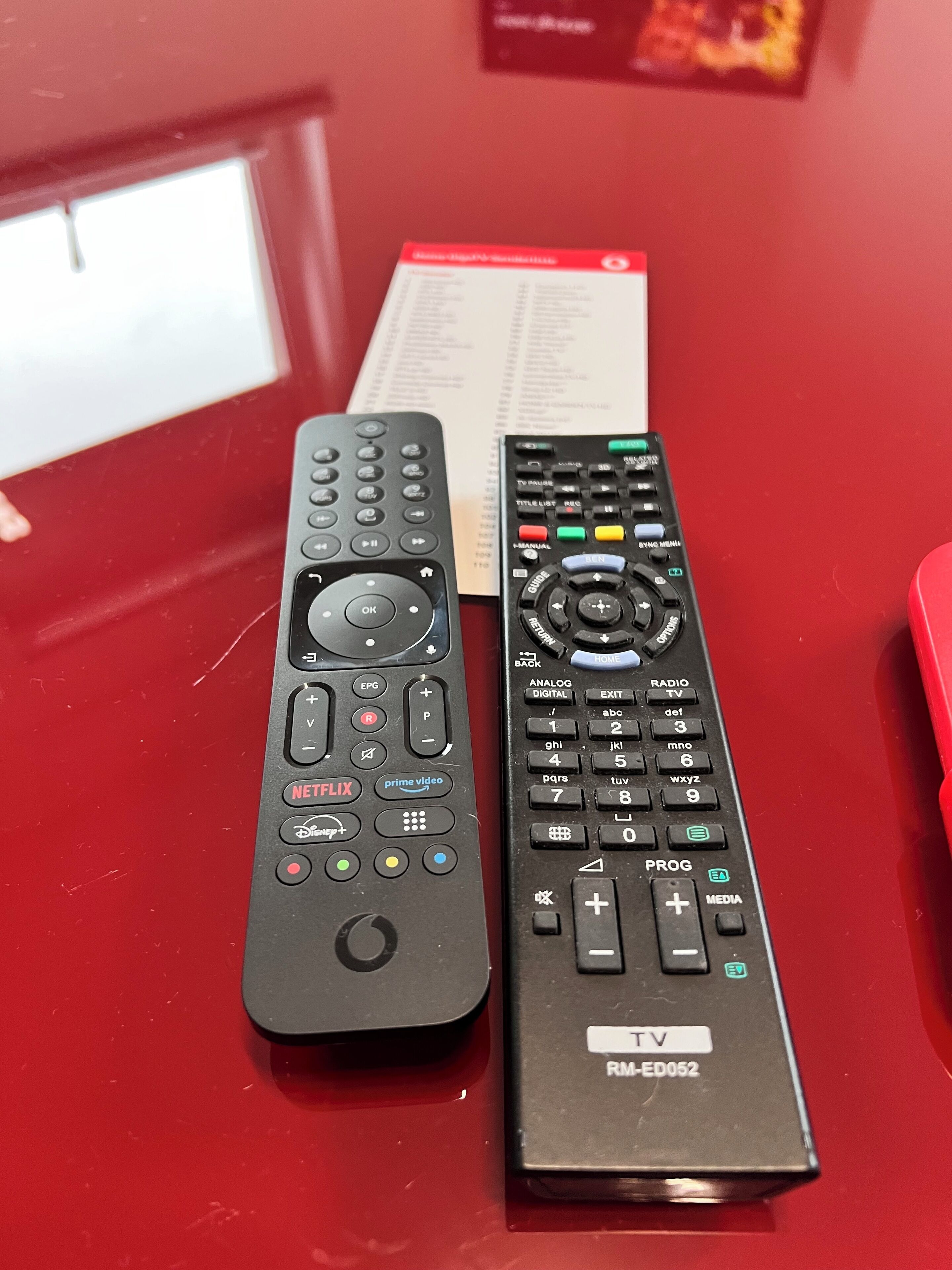 Deux télécommandes sur une surface rouge, avec une carte de menu en arrière-plan.