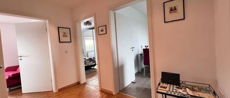 A room with wooden flooring, a bed with a red cover, a desk with a chair, and a framed picture on the wall.