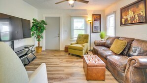 Ein Wohnzimmer mit Fernseher, Deckenventilator, Sofa, Sessel und einer Zimmerpflanze.