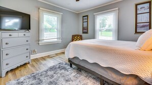 Ein Schlafzimmer mit Bett, Kommode, Deckenventilator und zwei Fenstern mit Jalousien.