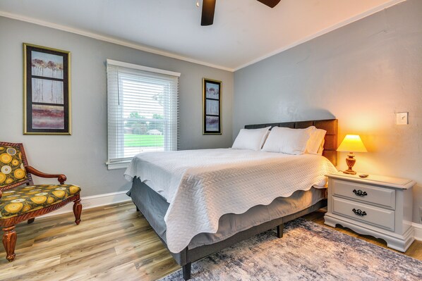 A bedroom with a bed, bedside table, lamp, chair, and artwork on the wall. - Home 1 Mi to Dtwn & High Point University! (High Point)
