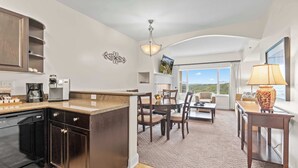 A modern kitchen with a central island, dining area with chairs and a table, and a view through large windows.