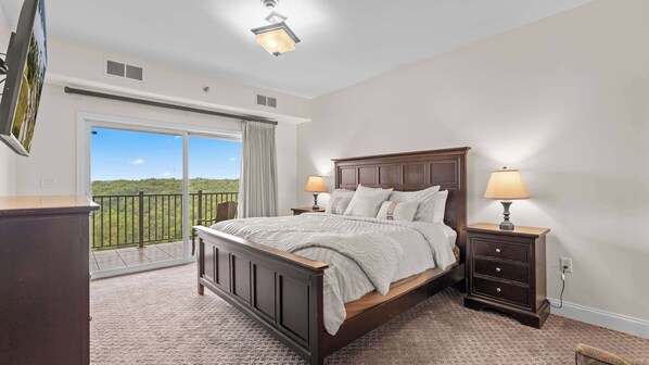 A bedroom with a large bed, two bedside tables with lamps, a sliding glass door to a balcony, and a ceiling light fixture.