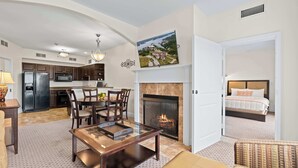 A spacious living area with a fireplace, a dining table, and a kitchen in the background.