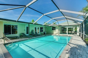 A swimming pool with a covered patio area, lounge chairs, and a clear blue sky.
