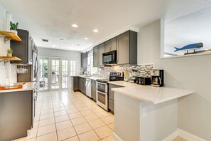 A modern kitchen with grey cabinets, a white countertop, and a microwave. There is a window with a view of greenery outside.