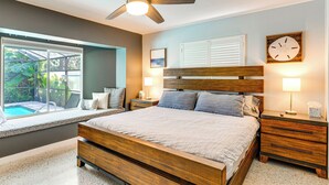 Ein Schlafzimmer mit einem großen Bett, einem Holzkopfende, zwei Nachttischen mit Lampen, einem Deckenventilator und einem Fenster mit Blick auf einen Pool.