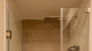 Chuveiro moderno com porta de vidro, piso de madeira e porta-toalhas.