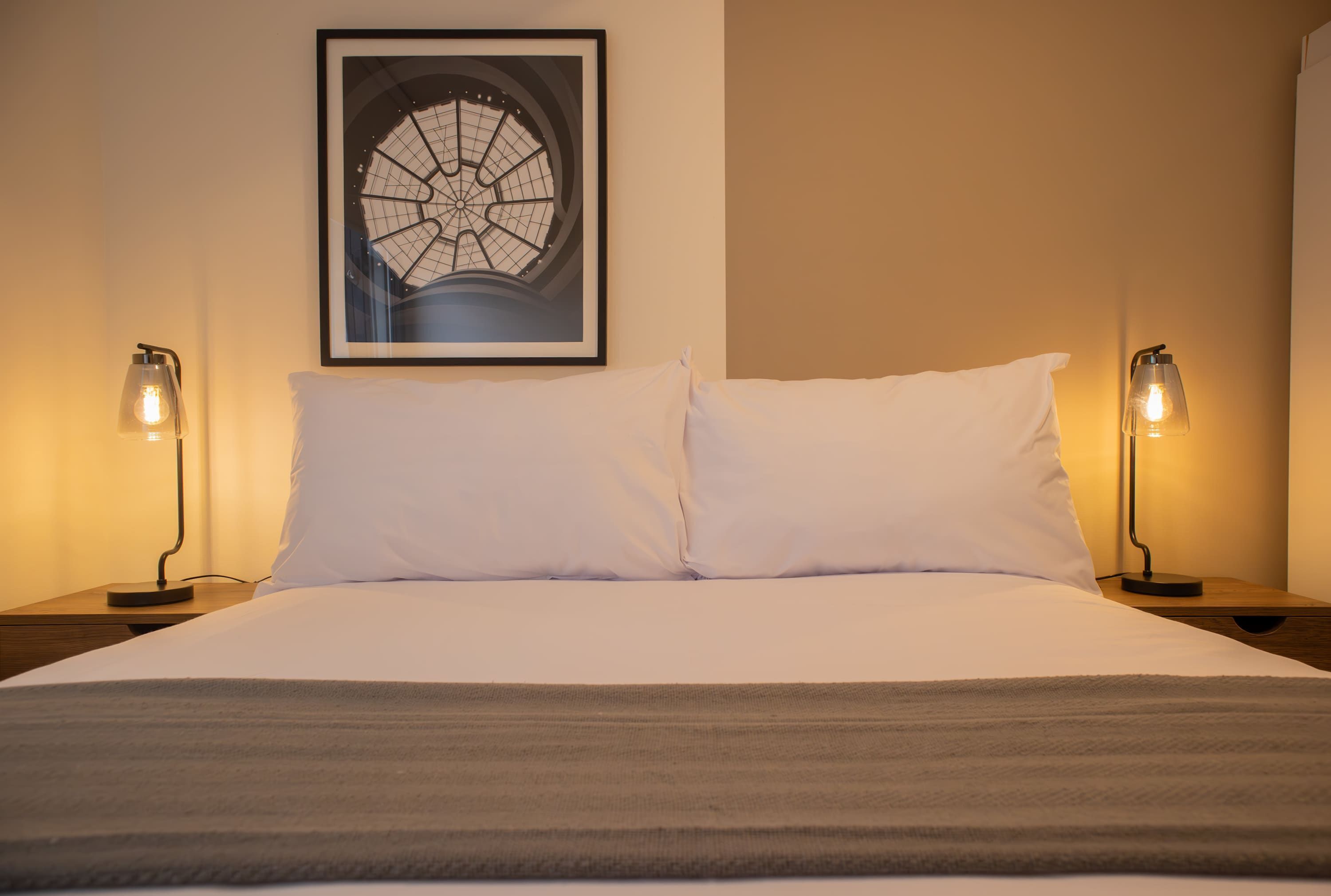 A neatly made bed with white linens, two bedside lamps, and a framed picture on the wall.