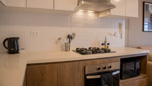 Uma cozinha moderna com armários brancos, coifa de aço inoxidável, forno embutido e micro-ondas.