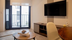 Uma sala de estar moderna com uma televisão de tela plana na parede, uma mesa de centro de madeira, uma poltrona confortável e uma porta de vidro deslizante que dá para uma varanda.