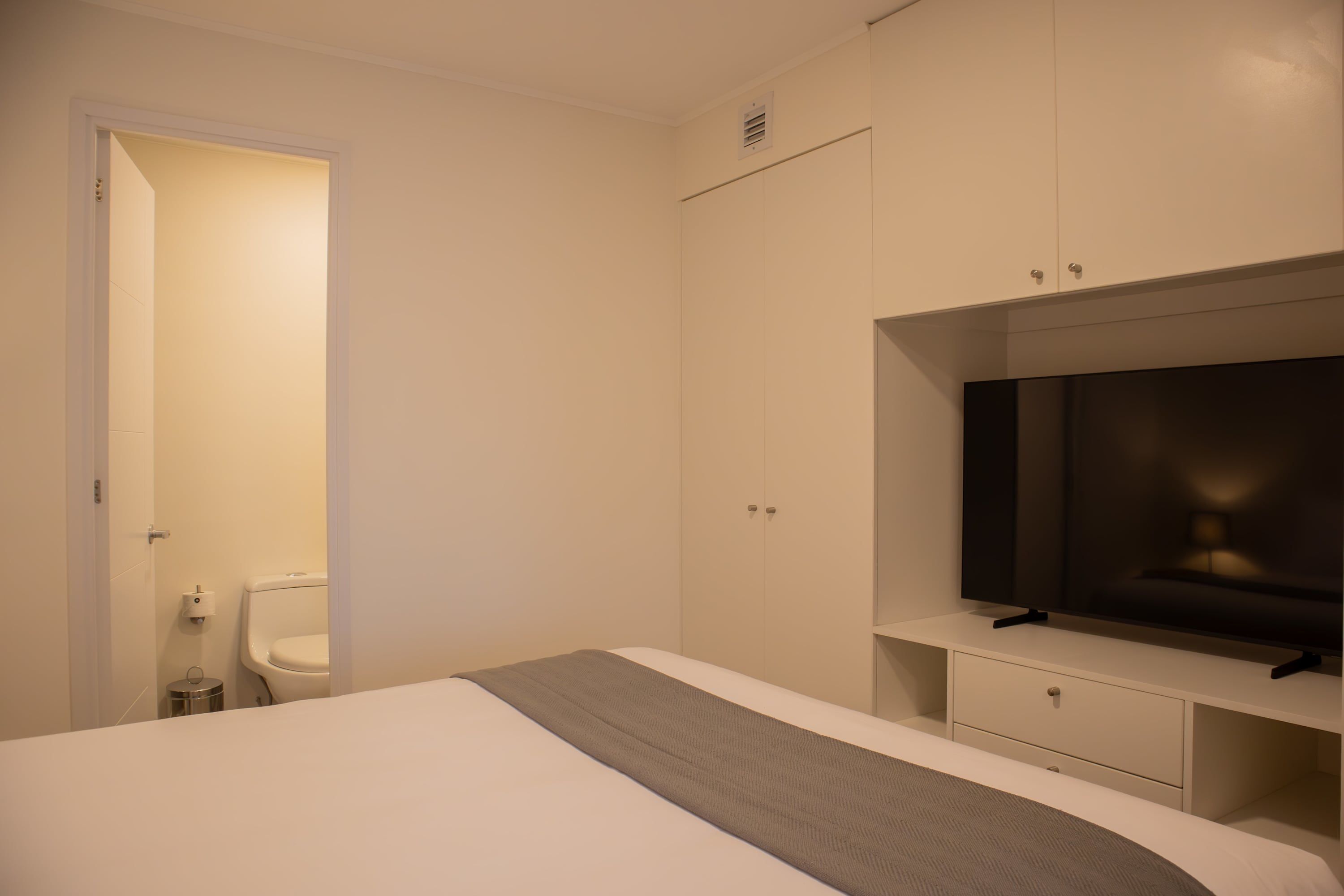 A bedroom with a bed, a TV, a wardrobe, and a toilet.