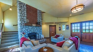 A spacious living area with a stone fireplace, comfortable seating, and a view through large windows.
