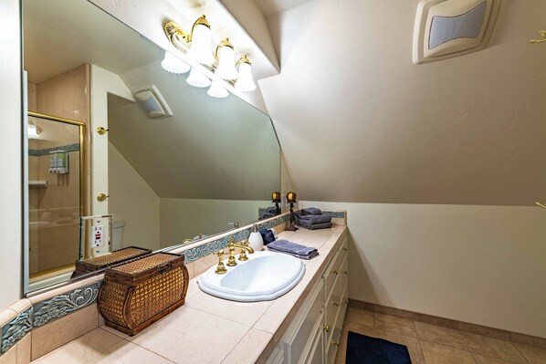 A bathroom with a large mirror, a sink, and a vanity with drawers. There are towels and a basket on the counter.