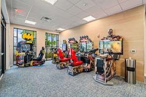 Una habitación con juegos de arcade, incluyendo máquinas temáticas de Batman y Terminator, y un ventanal con vistas a palmeras.