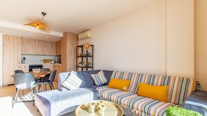A modern living room with a sofa, chairs, a coffee table, and a kitchen area in the background. - Apartment 'Vistamar 96' with Sea View, Wi-Fi and Air Conditioning (Benitachell)