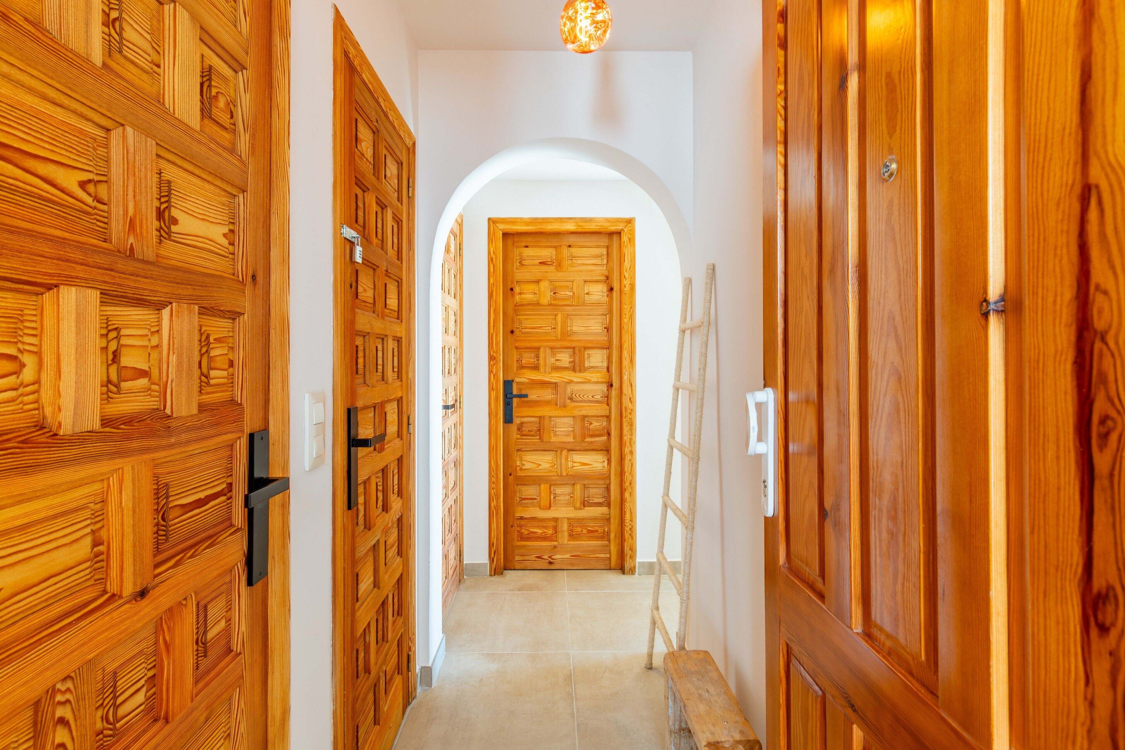 Un pasillo con puertas de madera y un arco blanco que da a una habitación.