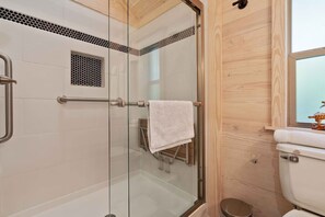 A modern bathroom with a glass shower enclosure, a wooden wall, and a white toilet.