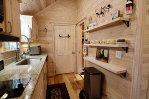 A compact kitchen with wooden walls, a granite countertop, a stainless steel sink, and a built-in oven.