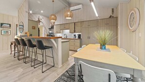 Une cuisine moderne avec des meubles en bois, un îlot central doté de tabourets de bar, un éclairage suspendu et une table à manger avec des chaises.