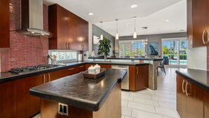A modern kitchen with dark wood cabinets, a central island, and a large window providing natural light. - PGA West #41 3 BD/3 BA, 2,400 sf - 31+ Night Minimum Bookings Available (La Quinta)