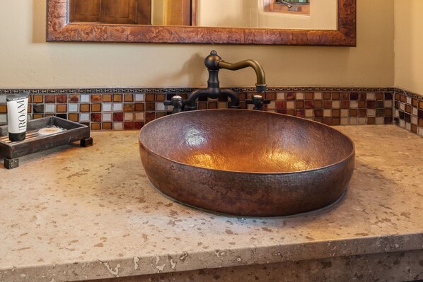 A copper sink with a vintage faucet, a soap dispenser, and a tray with a bottle of soap.
