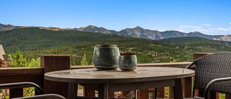 A round table with two ceramic pots and a wicker chair, overlooking a mountainous landscape.