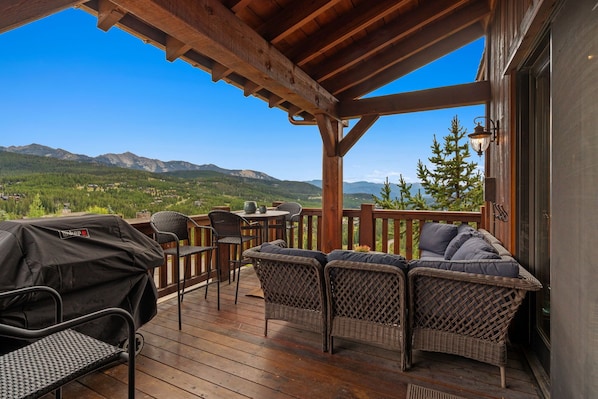 A wooden deck with wicker furniture, a grill, and a view of mountains.