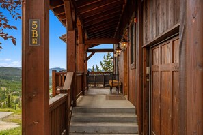 A wooden covered porch with a number '5B' sign, a concrete staircase, and a view of a mountainous landscape.