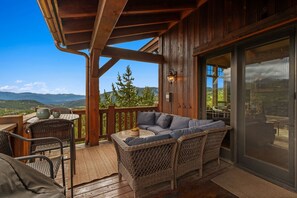 Une terrasse en bois avec des meubles en osier, une porte vitrée et une vue sur les montagnes.