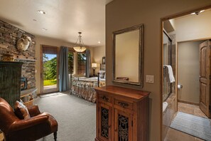 Une pièce spacieuse avec une cheminée en pierre, un grand miroir, un meuble en bois et un lit donnant sur l’extérieur.